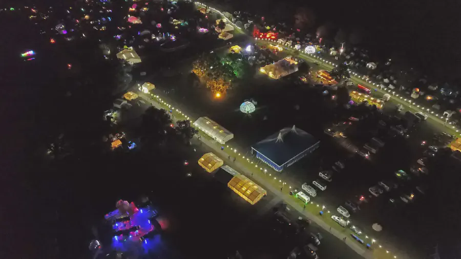 An aerial photograph of [EMF camp](https://www.emfcamp.org/) at night showing lit up pathways, big tends, and a glowing purple tent.