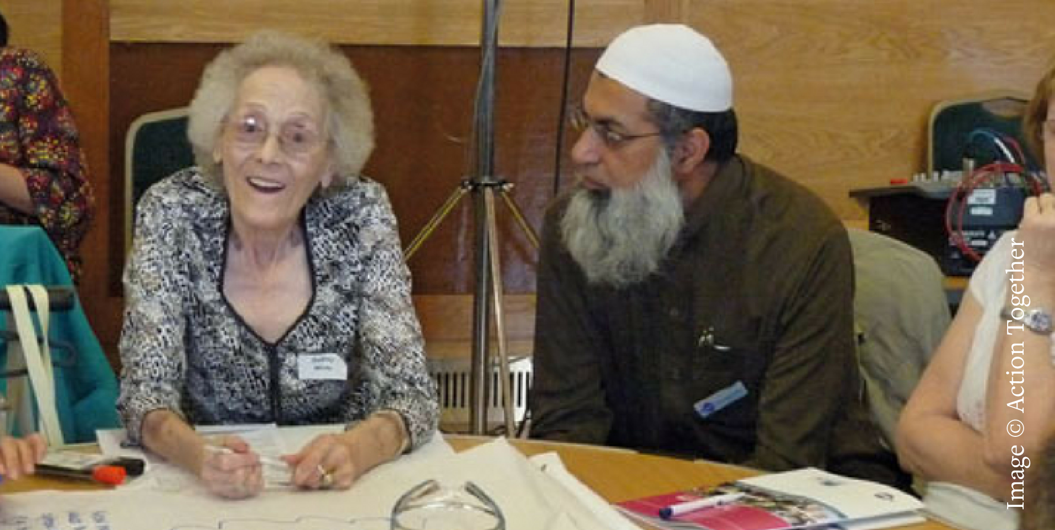 A white older woman and a brown muslim man sat around a table.